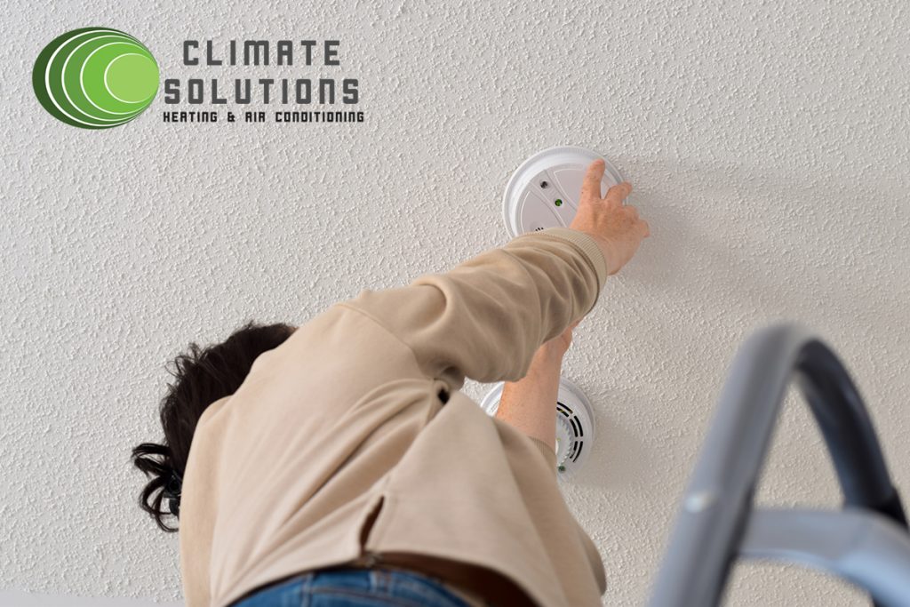 Woman reaching up for smoke alarm on ceiling at home